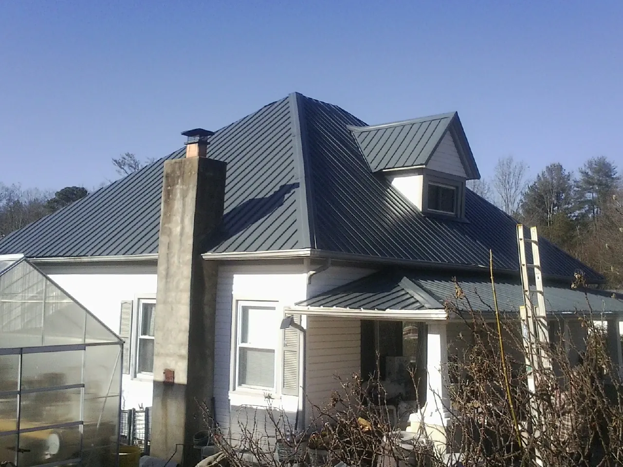 Dark blue standing seam metal roof on a white farmhouse with dormer — Slate & Tile Roof Repair by Roofing Brothers in Starbuck
