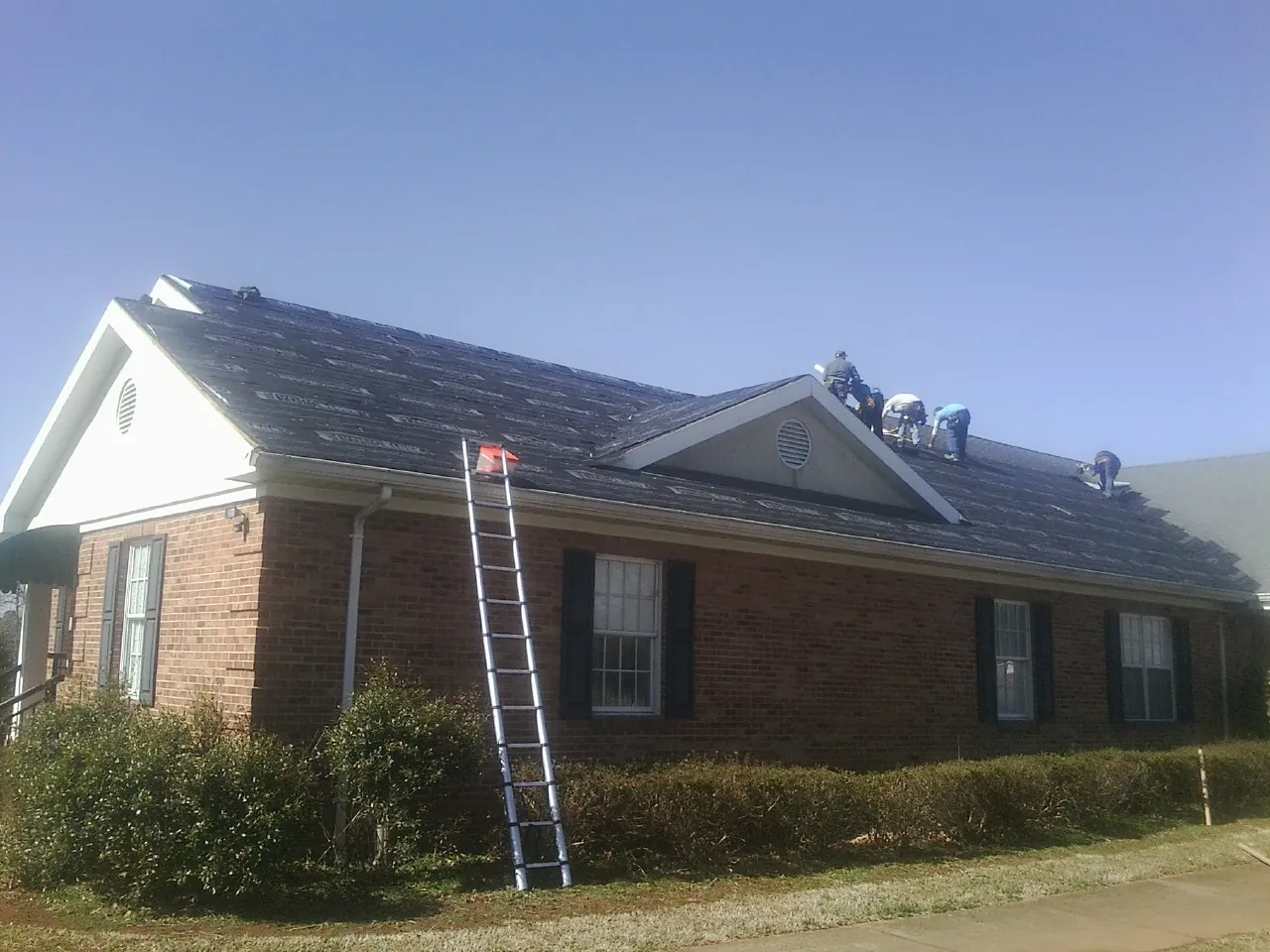 Crew tearing shingles off a brick ranch roof with a ladder set — Emergency Roof Repair work by our crew in Starbuck
