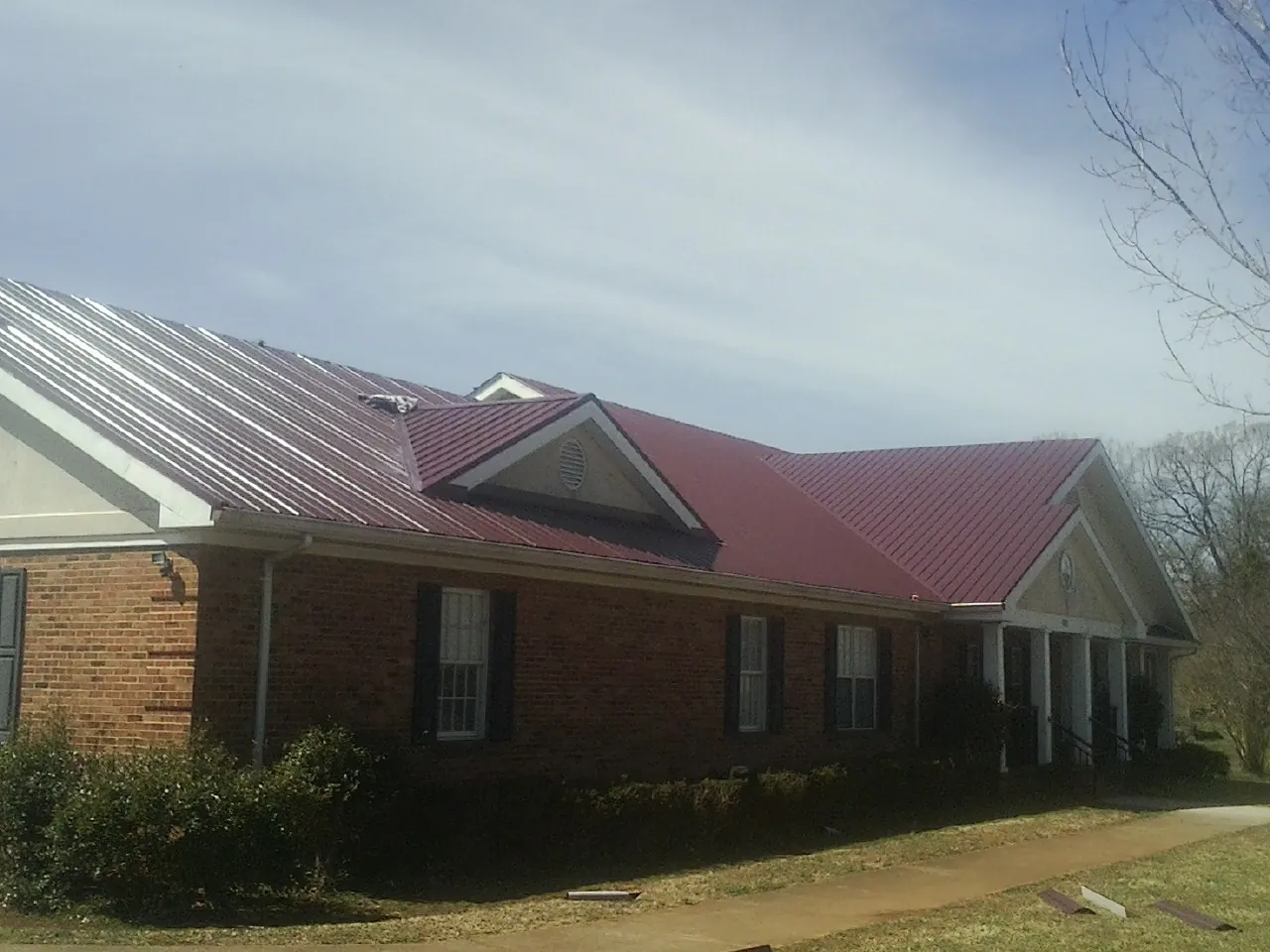 Red metal roof with gabled entries on a long brick building, from a Hail Damage Roof Repair job in Starbuck