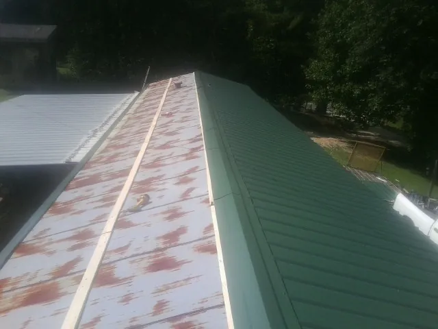 Old rusted panels beside newly installed green metal roofing — Wind Damage Roof Repair by Roofing Brothers in Starbuck