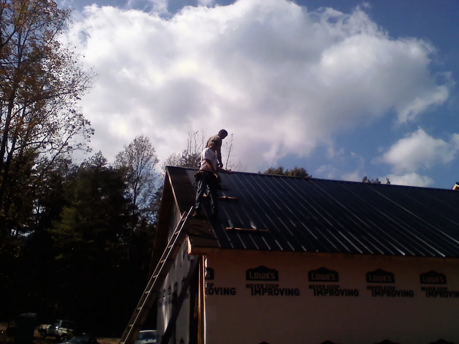 Roofer fastening dark metal panels high against a cloudy sky, from a Roof Inspection job in Starbuck
