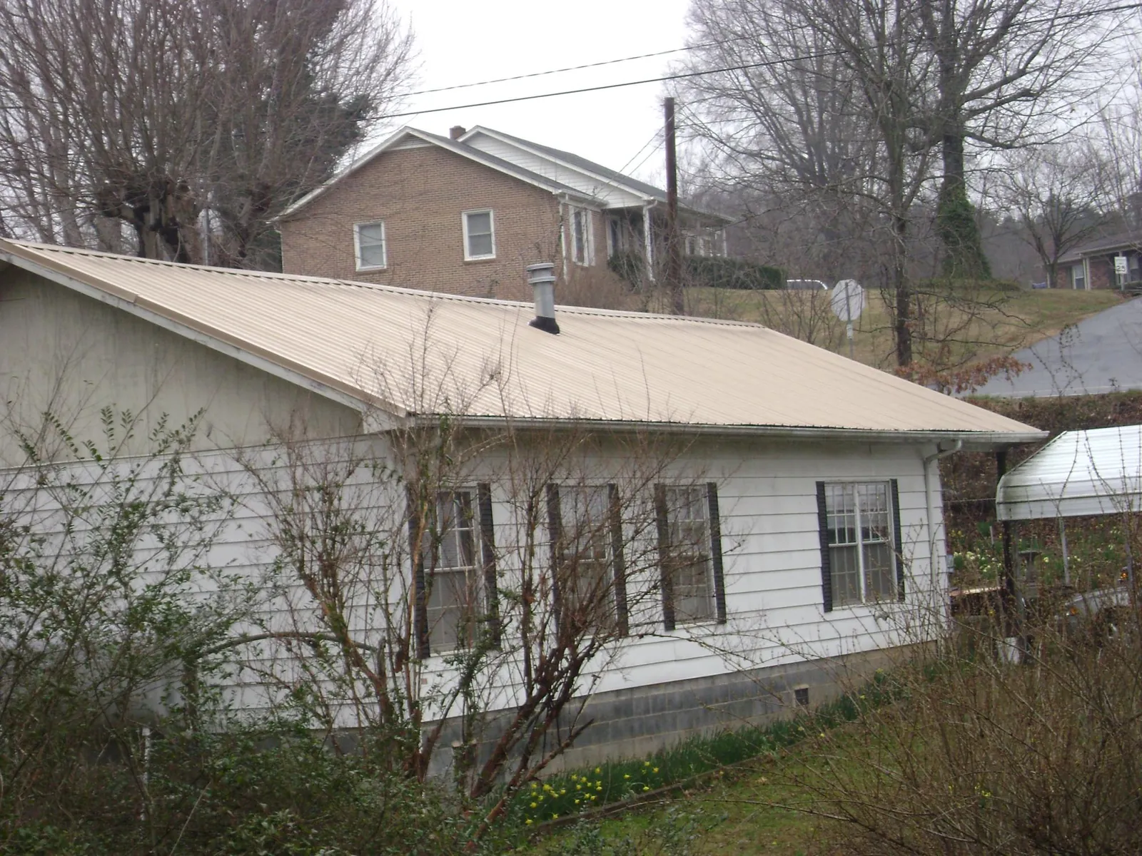 Tan metal roof on a white sided house set into a hillside — Commercial Roofing by Roofing Brothers in Starbuck